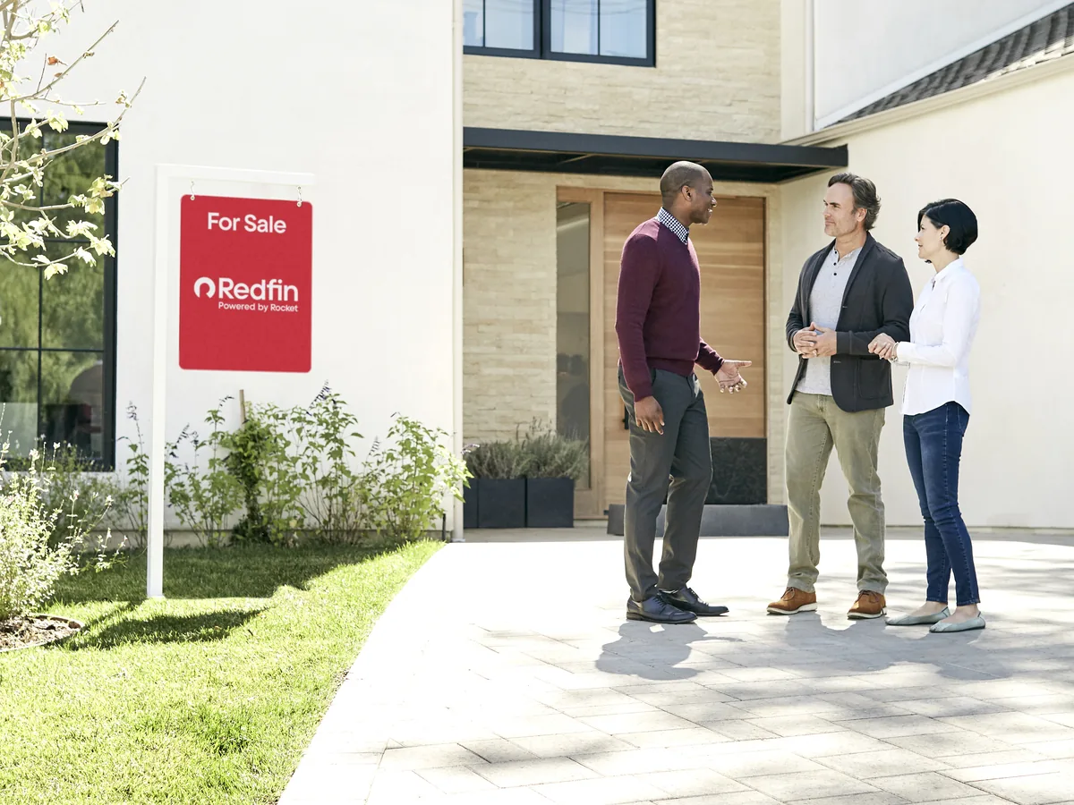 Buyers walking up to a new construction home with a Redfin for sale sign in the yard
